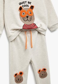Lysgrå hættejakke og sweatpants sæt med et bjørne-tryk, der har orange briller og ører, accentueret med en orange snor.