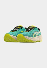 Παπούτσια ορεινού τρεξίματος σε τιρκουάζ και κίτρινο, με επάνω μέρος από δίχτυ, παχιά σόλα και υφή στην εξωτερική σόλα για καλύτερο κράτημα. Μαύρες λεπτομέρειες στα κορδόνια.