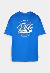 Zila īsām piedurknēm t-kreka, izgatavota no kokvilnas, ar lielu baltu grafiku, kas ietver "Nike Golf" un tekstu iekš dotētā aplī.