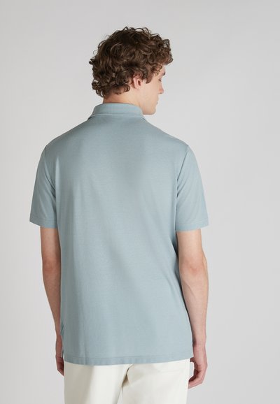 Polo shirt bleu clair à manches courtes avec col, texture lisse et ourlet droit. Une légère fente sur le côté près de l'ourlet ajoute une touche de détail.
