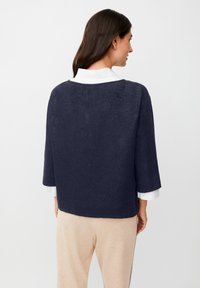 Maglione blu navy corto con maniche tre quarti, realizzato in tessuto testurizzato, con scollatura tonda e vestibilità relax sopra pantaloni beige.