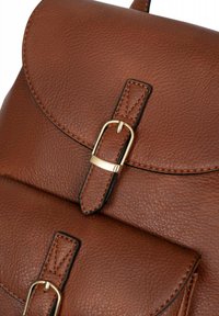 Bruine leren rugzak met een gestructureerd oppervlak, voorzien van een ronde flap, goudkleurige gesp details en zwarte stiksels.