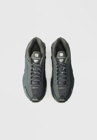 Nike Shox αθλητικά παπούτσια σε σκούρο γκρι, με πλέγμα στην επάν�ω πλευρά, υφασμάτινες λεπτομέρειες και μαλακό κολάρο. Ο δεσμός και το λογότυπο είναι ορατά στον γλωσσίδιο.