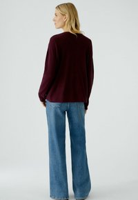 Bordeauxfarbener, gestrickter Pullover mit langen Ärmeln, lockere Passform, kombiniert mit hellblauen, weit geschnittenen Jeans. Schlichte Textur, entspannte Gestaltung.