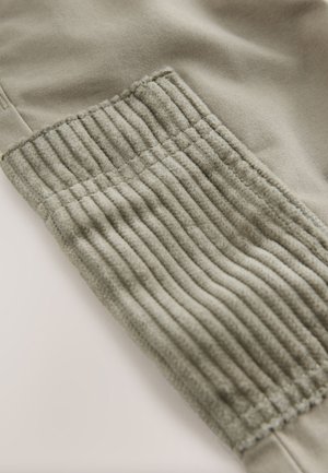 Lichtgrijs katoenmixstof met een gestructureerd geribbeld paneel bij de enkel. Gladde oppervlakte met zichtbare stiksels en elastische accenten.