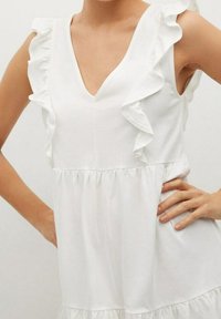 Weißes Kleid mit V-Ausschnitt, ausgestattet mit gerafften Ärmeln und einem gestuften, gerafften Oberteil. Weiches Baumwollmaterial mit einer glatten Textur.