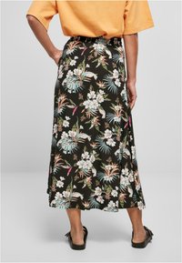 Blomsterkjole i sort med fargerike tropiske mønstre, med en rynket midje og et flytende, midt-langt design. Kombinert med svarte sandaler.