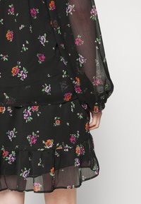 Vestido negro transparente con pequeño estampado floral en morado, naranja y rosa, que presenta mangas largas y un dobladillo con volantes.