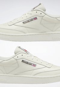 Ett par vita Reebok lädersneakers med logotyp och brittisk flagga på sidan, visade mot en enkel vit bakgrund.