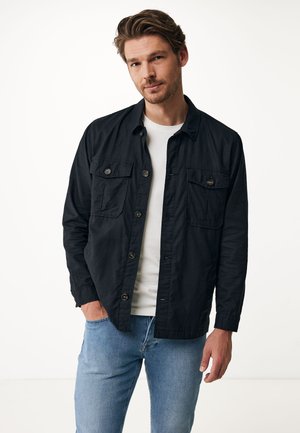 Zwarte overhemd met twee borstzakken, lange mouwen en een gladde stoftextuur, gedragen over een wit T-shirt en gecombineerd met lichtblauwe jeans.
