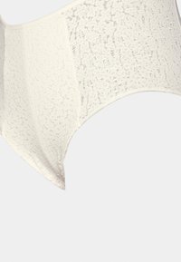 Lace bralette in cream with floral pattern. Soft, sheer material, seamless design, wide band, and round neckline. Textured surface.