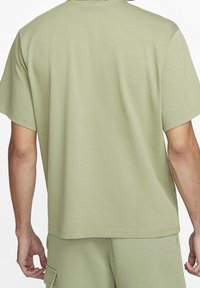 Mężczyzna w jasnogreen koszuli z krótkim rękawem i dopasowanych szortach cargo, pokazany od tyłu na białym tle.