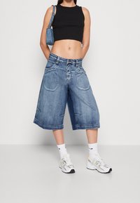 Denim culotteshorts med lös passform, ljusblå tvätt, två framfickor och kontrasterande sömmar; ihop med en svart crop top och vita sneakers.