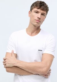 Valge lühikeste varrukatega särk, mis on valmistatud pehmest puuvillast. Särgil on must "BOSS" logo vasakul rinnal ning klassikaline ümar kaelus.