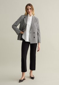 Blazer de cuadros en blanco y negro, de doble botonadura, camisa blanca, pantalones negros ajustados y bailarinas negras de punta. Tejido suave, corte entallado.