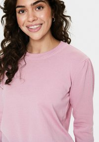 Pull en tricot rose clair avec encolure côtelée et manches légèrement bouffantes. Le tissu semble lisse avec une texture fine.