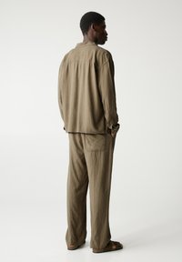 Set de cămașă și pantaloni, de culoare verde măslinie, cu croială lejeră, realizat dintr-un material texturat. Cămașa are guler și manșete cu nasturi; pantalonii dispun de buzunare laterale.