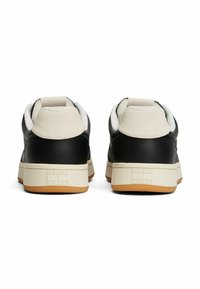 Czarne skórzane sneakersy z białą sztuczną podszewką z owczej wełny i kremowymi akcentami; mają teksturowaną podeszwę i metkę z logo na pięcie.