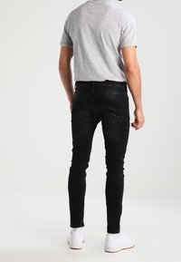 Vaqueros negros de denim con un ajuste slim, que cuentan con bolsillos traseros, combinados con una camiseta gris de manga corta y zapatillas blancas. Textura suave.
