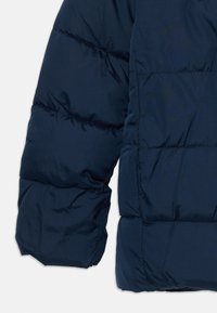 Manche et côté d'une veste matelassée bleu marine, montrant des sections rembourrées horizontales cousues et une texture de tissu lisse.