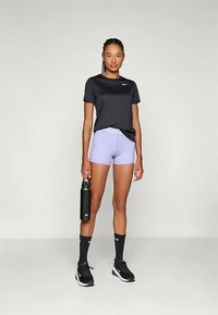 Černé sportovní tričko, světle fialové šortky, černé tenisky, černá láhev na vodu. Krátké ponožky s bílými akcenty. Jednoduché, funkční sportovní oblečení.