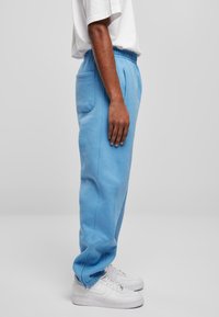 Lichtblauwe joggingbroek van zacht materiaal, met een tailleband met trekkoord, zijzak en taps toelopende broekspijpen, gecombineerd met witte sneakers.