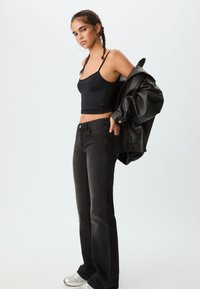 Top nero senza maniche, jeans neri svasati e giacca di pelle nera oversize con finitura testurizzata, abbinati a scarpe da ginnastica argento.