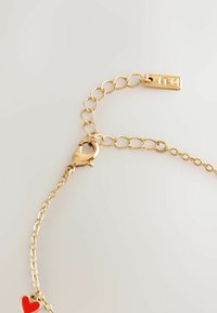 Gold chain bracelet featuring a lobster clasp, a series of linked metal circles, and a red heart charm attached. Smooth texture.