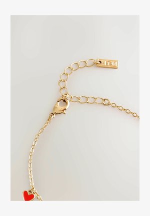 Kuldne käevõru, millel on lehviku tüüpi klamber, järjestikused lingitud metallringid ja küljes punane südaäkar. Sile tekstuur.