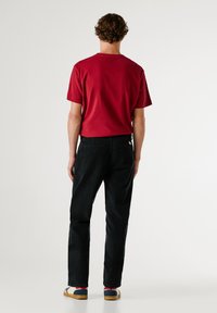 Rode katoenen t-shirt met korte mouwen en een ronde hals, gecombineerd met zwarte denim broek, beide weergegeven vanuit een achteraanzicht.