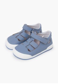 Zapatos de cuero azul claro con diseño recortado, correa de velcro, suela de goma blanca y acentos marrones en contraste. Adecuados para uso casual.