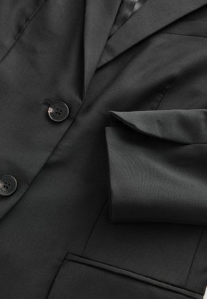 Blazer noir ajusté avec deux boutons noirs, un col cranté et une poche poitrine simple. Texture lisse, design formel.