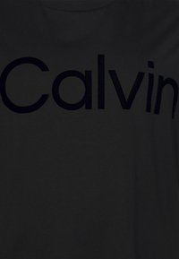 Camiseta de algodón negra con el texto grande "Calvin" en negro en el pecho. Textura suave con un cuello redondo clásico. Diseño sencillo.