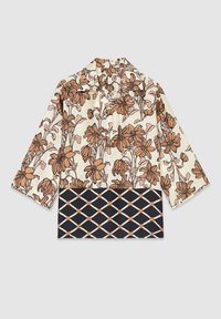 Blusa a fiori nei toni crema e marrone, con maniche a tre quarti. La parte inferiore presenta un motivo geometrico nei toni navy e pesca.