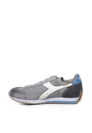 Scarpa sportiva grigia con una finitura liscia e metallica, dettagli bianchi e un tallone nero texturizzato. Presenta un design con lacci e suola in gomma.