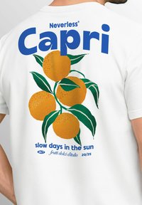 Weißes T-Shirt mit einem lebendigen Grafikdesign von Orangen und grünen Blättern, mit fettem Text "Capri" und einem Slogan darunter.
