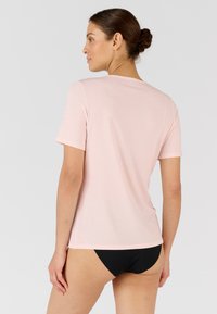 T-shirt corto a maniche corte di colore rosa chiaro con scollatura rotonda e una texture liscia e morbida. La vista posteriore mette in evidenza una forma aderente.