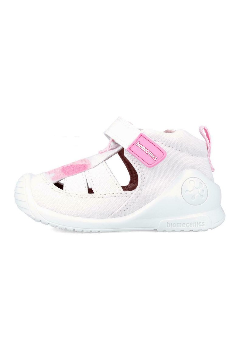 Zapatilla de lona blanca con acentos rosas, que presenta un diseño de parte trasera cerrada, tira de Velcro y un diseño troquelado para mayor transpirabilidad. Suela de goma para un buen agarre.