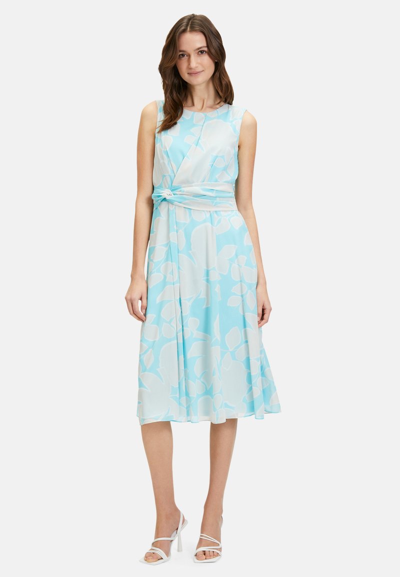 Hellblaues, ärmelloses Kleid mit weißen Blumenmuster, geknotetem Taillendetail und fließendem Rock. Glattem Stoff mit weicher Textur.