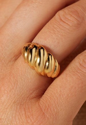 Gold ring featuring a twisted design with smooth, reflective surfaces. It wraps around the finger with rounded edges and a polished finish.