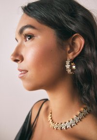 Cercei hoop de culoare aurie, cu un model în stele, și un colier asortat cu accente în formă de stea. Textură metalică netedă, finisaj strălucitor.