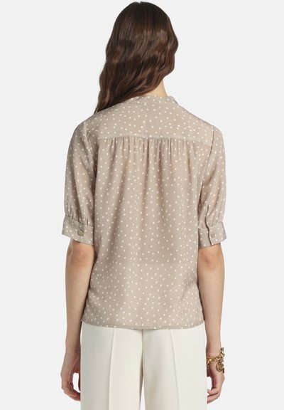 Bluza kratkih rokavov v svetlo bež barvi z belimi pikami, z naborki na hrbtni strani in zavihanimi manšetami. Gladek, lahek material.