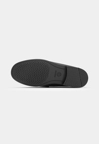 Schwarze Schuhsohle mit strukturiertem Gummi für Halt, mit einer glatten Kante und Logodetail an der Ferse. Entwickelt für Komfort und Langlebigkeit.