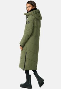 Lange olijfgroene gewatteerde jas met een capuchon, ritssluiting aan de zijkant en zwarte accenten. Kenmerkt zich door een geweven ontwerp en wordt gecombineerd met zwarte kniehoge laarzen.