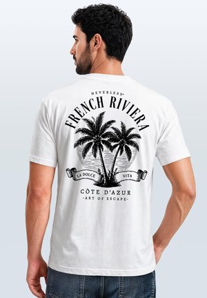 Man wearing white t-shirt with black palm tree graphic and French Riviera text on back, standing against a plain light background.