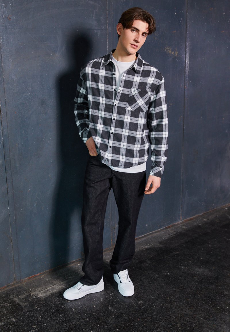 Sort og hvid ternet flannel skjorte med brystlomme, lagdelt over en hvid t-shirt; parret med mørke jeans og hvide sneakers.