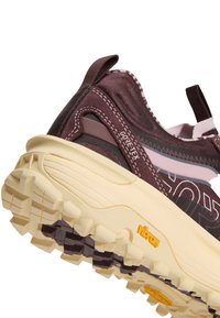 Gros plan d'une chaussure de plein air violette et beige en tissu Gore-Tex avec une semelle en caoutchouc Vibram montrant des motifs de crampons profonds.