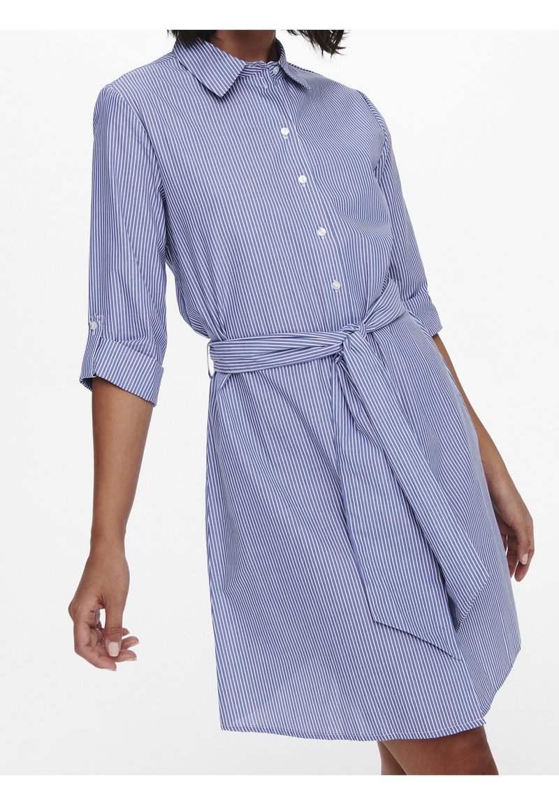 Abito camicia a righe blu e bianche con colletto, chiusura con bottoni davanti e maniche a lunghezza gomito. Include una cintura coordinata in tessuto. Texture liscia.