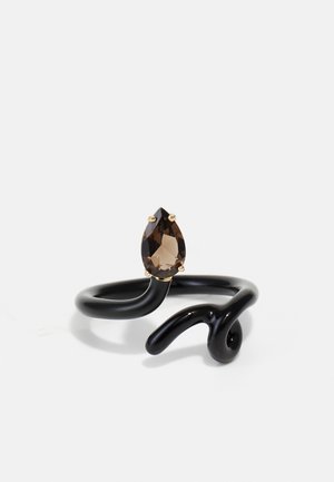 Anello in metallo nero con un design intrecciato e una gemma marrone a forma di pera, accentuata in oro, al centro.