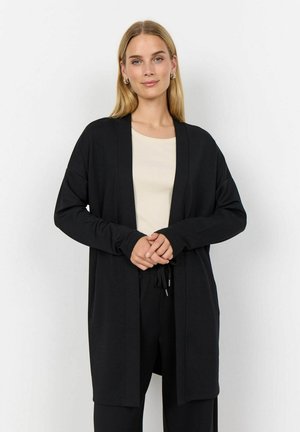 Zwarte cardigan met open voorkant, lange mouwen en een relaxte pasvorm. Gemaakt van een gladde stof, gelaagd over een beige top. Eenvoudig ontwerp, geen patronen.